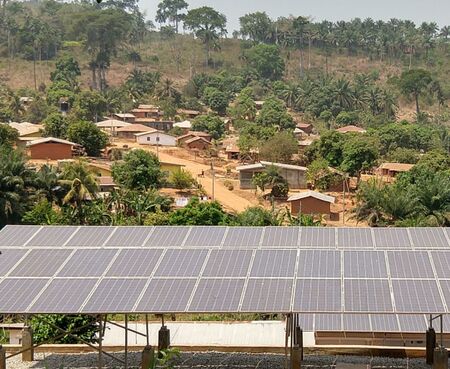 Image of approximately 30 solar panels in the foreground with a rural Tanzanian village and the nearby environment in the background. Mini-grids may provide rural communities with clean, cheap, and reliable energy.