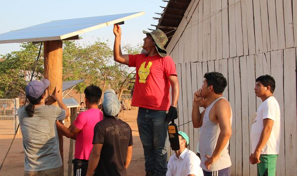 Photo by Neal Hegarty Photograph of eight men from the Xingu Indigenous Park installing a solar panel in the village of Pyulaga in the Brazilian Amazon.